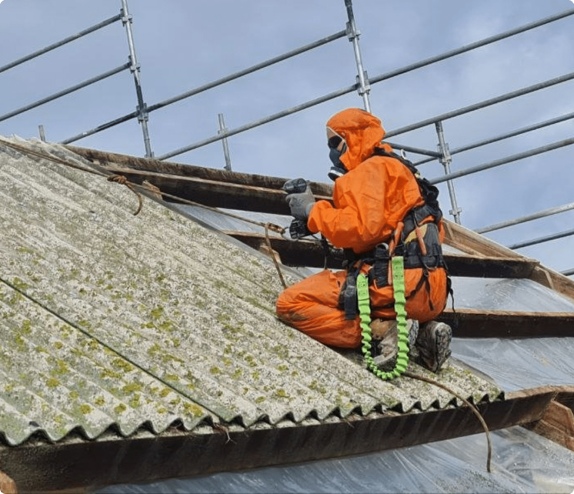 A worker in PPE removes asbestos roofing material.