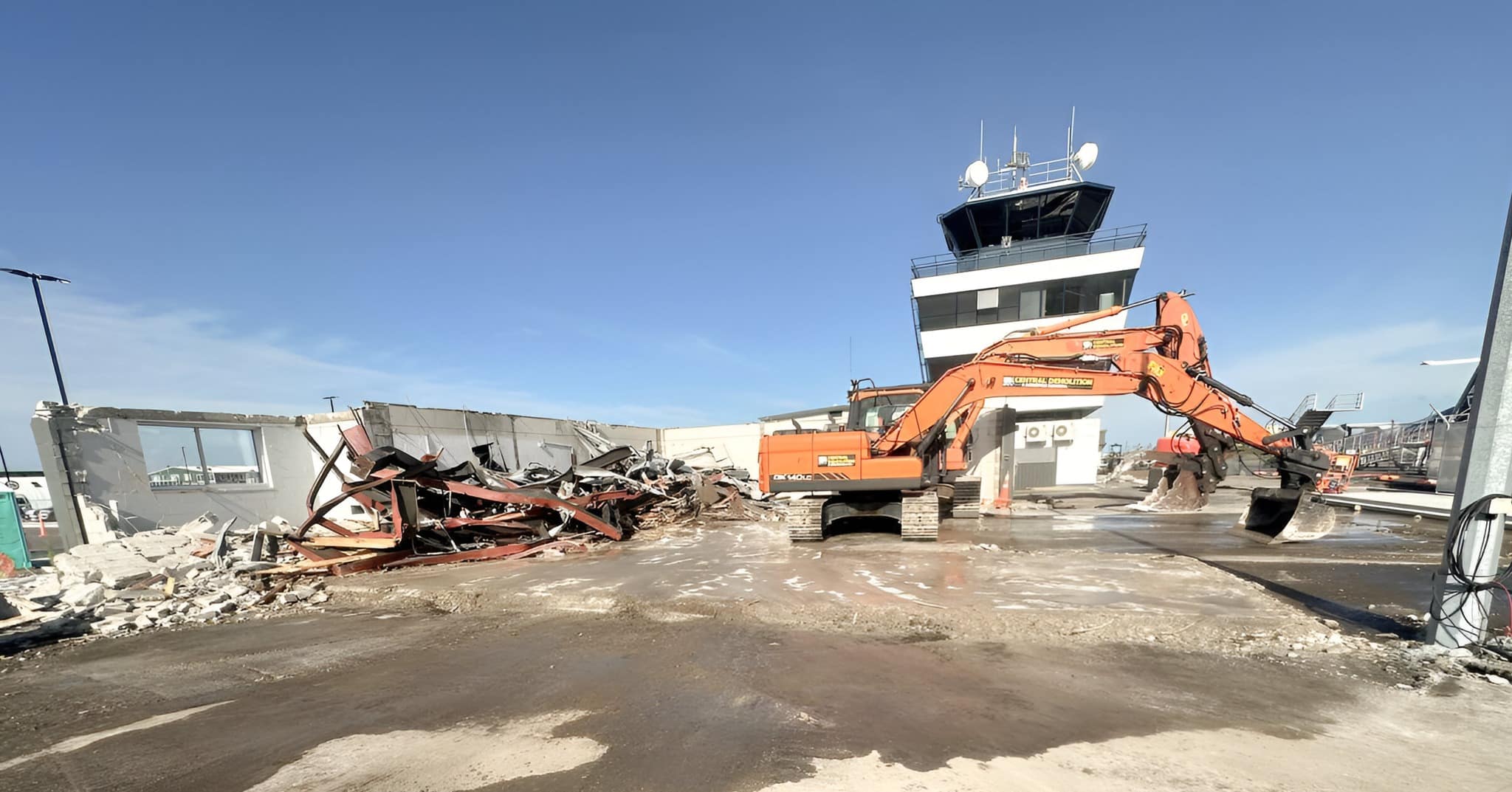 Two diggers in front of an air traffic tower during the Tauragana airport demolition project.